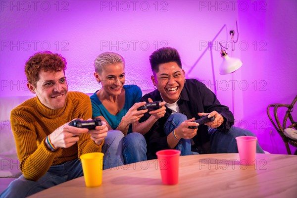 Group of young friends playing video games together on the sofa at home, purple led, having fun