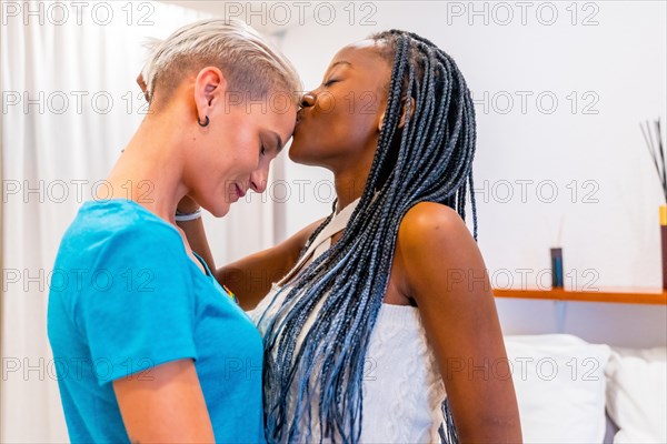 Beautiful lesbian couple kissing on the forehead on the bed at home interior, lgbt concept