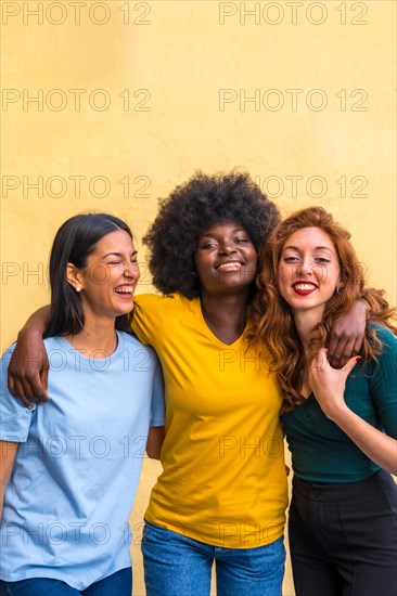 Portrait of beautiful multiethnic female friends smiling on a yellow wall having fun, copy paste