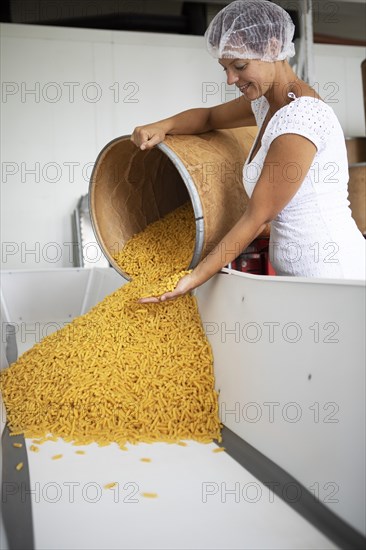 Woman with hair protection tipping noodles from a storage bin into a tub, Finkensteiner Nudelfabrik, Finkenstein am Faaker See, Villach region, Carinthia, Austria, Europe