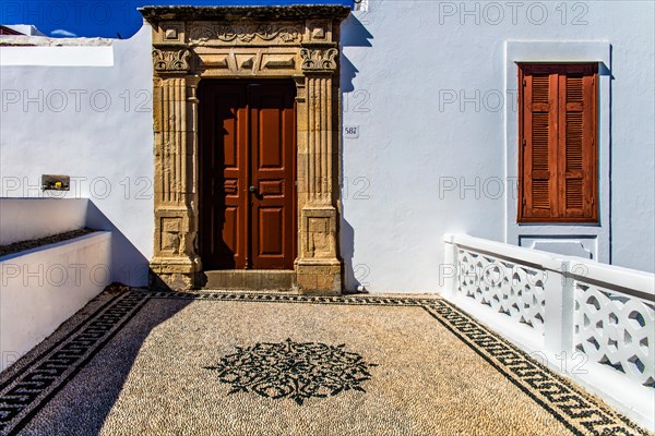 Old wooden doors with pebble mosaics on the floor, winding streets with white houses, Lindos, Rhodes, Greece, Europe