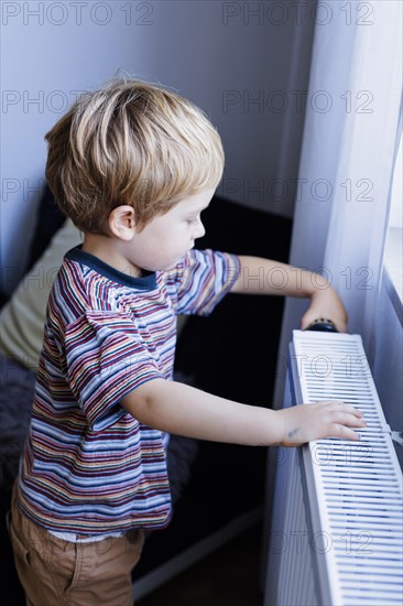 Bonn. Toddler turns the heating thermostat in the childrens room. Bonn, Germany, Europe