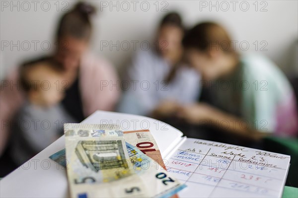 Household book with thirty-five euros. In the background a mother with three children., Bonn, Germany, Europe