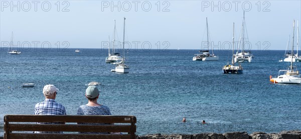 Seniors sitting on a wooden bench by the sea, Lanzarote, Canary Islands, Spain, Europe