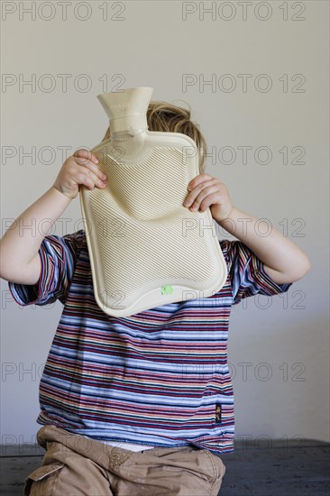 Bonn. Toddler hiding behind a hot water bottle. Bonn, Germany, Europe