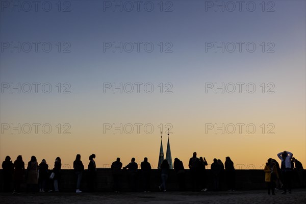 People standing on a viewing platform of the Kaiserburg Nuremberg at sunset. The towers of the Sebaldus Church can be seen behind. Nuremberg, 13.02.2023., Nuremberg, Germany, Europe