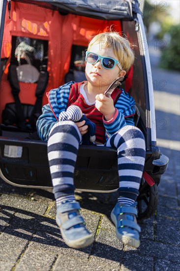 Toddler in trailer with sunglasses, enjoying autumn sunshine. Bonn, Germany, Europe