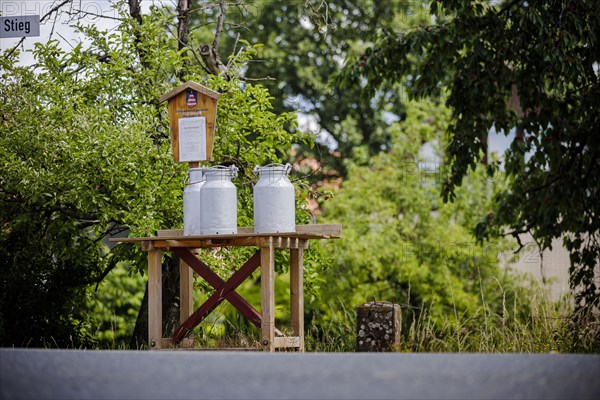 Milk cans stand for collection on a bench in the village of Mackenrode. Mackenrode, 28.06.2022, Mackenrode, Germany, Europe