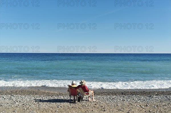 Older couple in sun hats on camping chairs on the beach, looking out over the turquoise Mediterranean Saint Maxime, Var, France, Europe