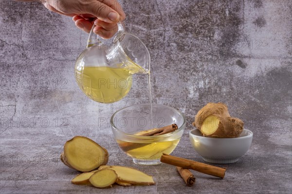 Womans hand pouring a cup of fresh ginger tea with cinnamon and lemon