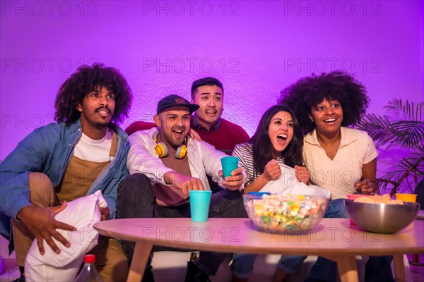 Adult party. Young people sitting on the sofa watching a football game with popcorn. Excitement for soccer