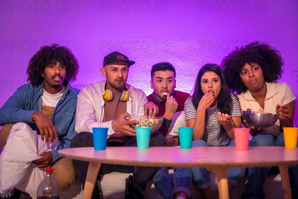 Young people sitting on the sofa watching a scary movie with popcorn. scared watching tv