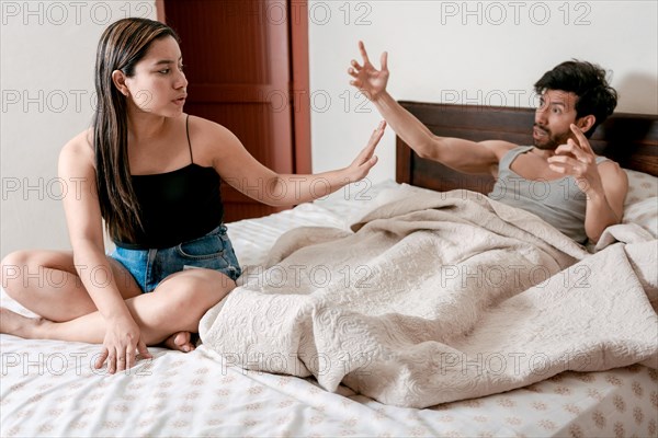 Husband fighting with his wife in bed. Upset wife with husband in bedroom bed