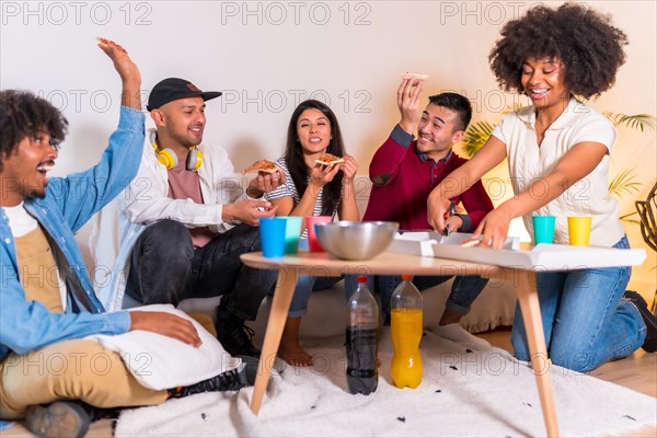 Group of multiethnic friends on a sofa eating pizza and drinking soft drinks at a home party