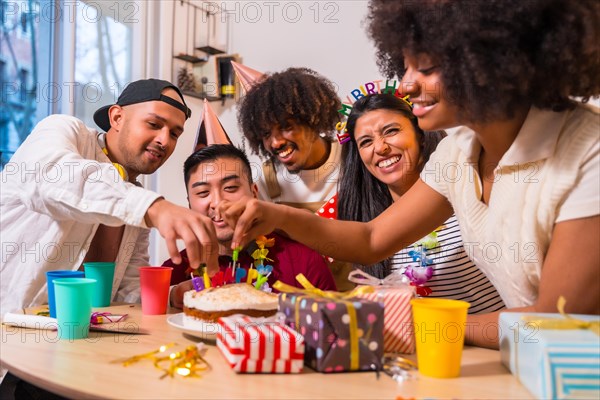 Multi-ethnic group of friends at a birthday party on the sofa at home with a cake and gifts