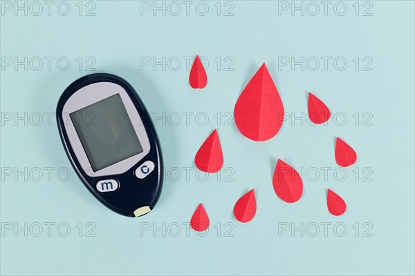 Blood glucose sugar meter device for diabetes illness next to paper blood drops
