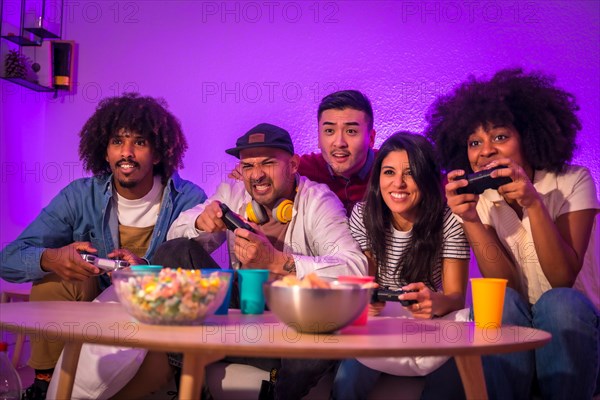 Adult party. Young people sitting on the sofa playing video games with popcorn. Joystick or controller in hand