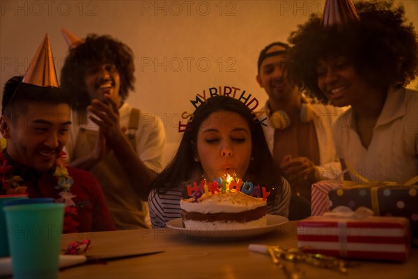 Multi-ethnic group of friends at a birthday party on the sofa at home with a cake and gifts