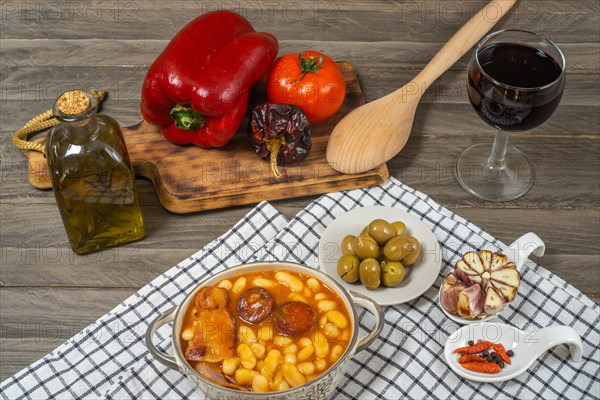 White beans stewed with bacon and chorizo in a ceramic pot on a wooden table with all the ingredients of the recipe