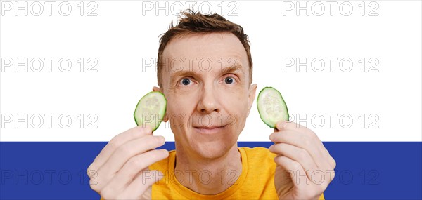Middle-aged man holds two slices of cucumber in hands