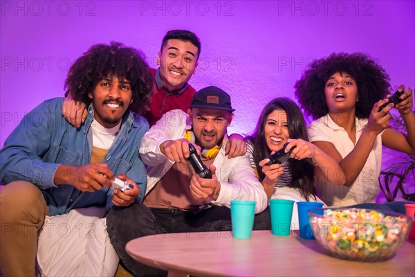 Adult party. Attractive young men sitting on the sofa playing video games with popcorn. Expressing joy while holding the joystick and looking at the monitor