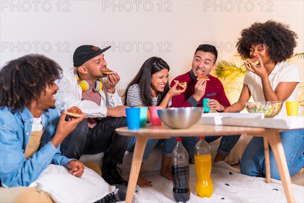 Group of multiethnic friends on a sofa eating pizza and drinking soda at a home party