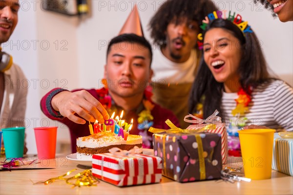 Multi-ethnic group of friends at a birthday party on the sofa at home with a cake and gifts