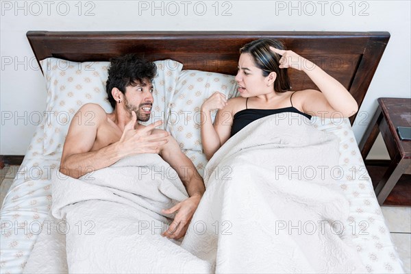 Upset couple lying in bed arguing. Top view of young couple lying in bed arguing. Marriage problems concept