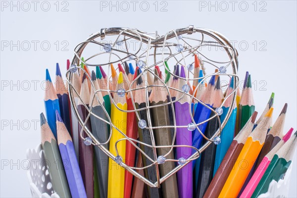 Color Pencils and heart shaped metal wire cage on a white background