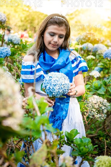 Beautiful Nicaraguan woman in national folk costume holding flowers in a nursery. Portrait of girl in traditional Central American folk costume holding flowers in a nursery. Nicaraguan folk costume