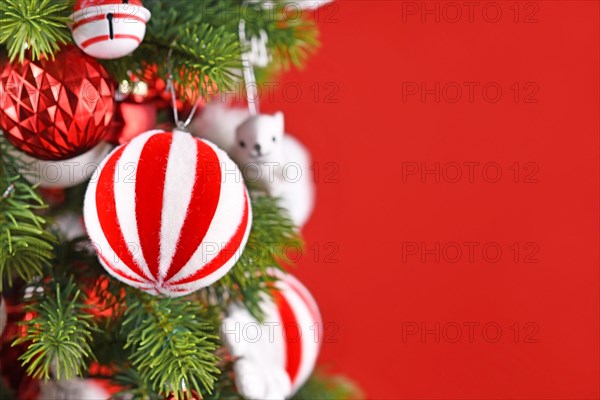 Striped Christmas ornament bauble hanging from tree branch in front of red background with copy space