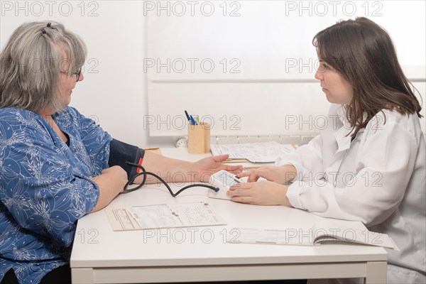 Young doctor taking her elderly patients blood pressure at the office