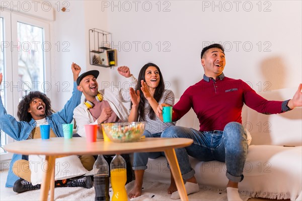 Group of multi-ethnic friends on a sofa eating pizza and drinking soft drinks at a home party