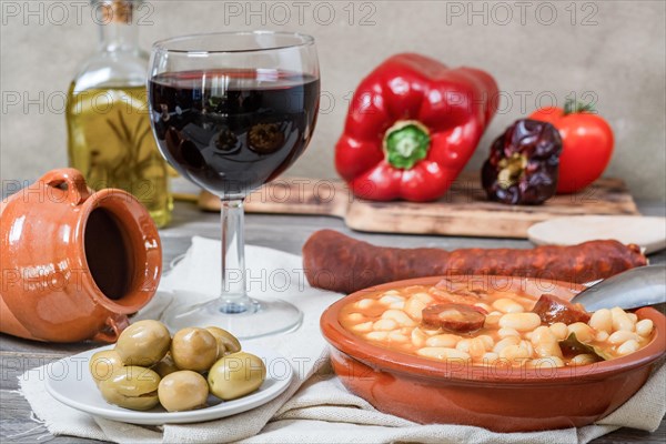 White beans stewed with bacon and chorizo in an earthenware casserole on a wooden table with all the ingredients of the recipe