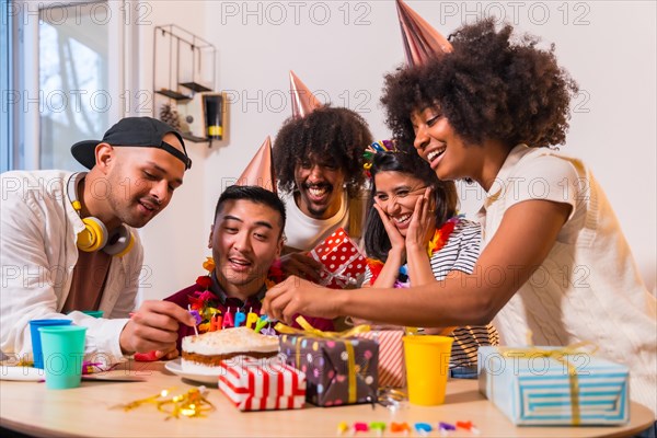 Multi-ethnic group of friends at a birthday party on the sofa at home with a cake and gifts