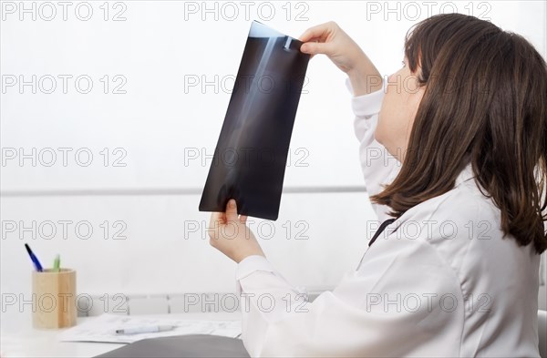 Young female doctor in profile looking at a patients x-ray with a white background
