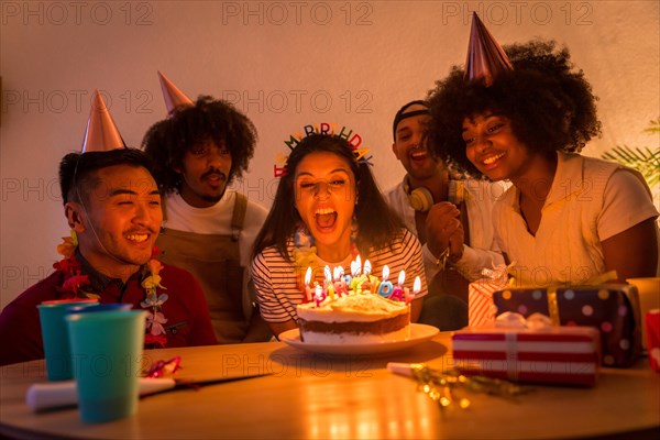 Multi-ethnic group of friends at a birthday party on the sofa at home with a cake and gifts