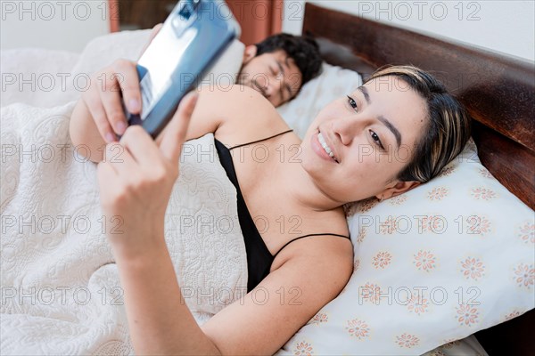 Unfaithful woman with phone while the man sleeps. Unfaithful girlfriend with phone while boyfriend sleeps