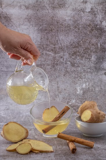 Womans hand pouring a cup of fresh ginger tea with cinnamon and lemon