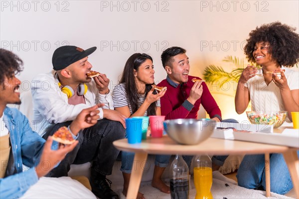 Group of multiethnic friends on a sofa eating pizza and drinking soda at a home party