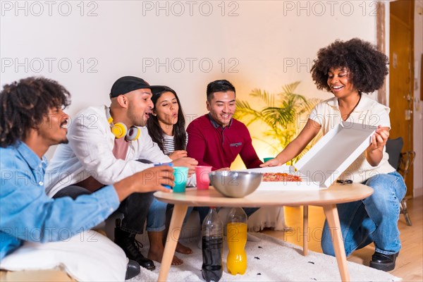 Group of multiethnic friends on a sofa eating pizza and drinking soft drinks at a home party