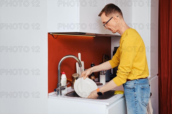 Middle-aged man washing plate after dinner in kitchen in the evening