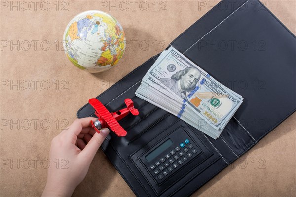 Hand holding model airplane beside globe and American dollars