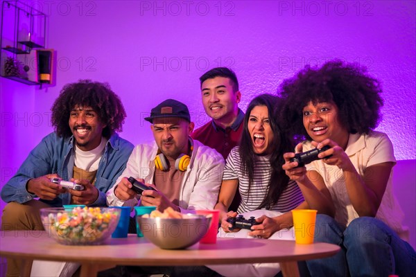 Adult party. Young people sitting on the sofa playing video games with popcorn. Joystick or controller in hand