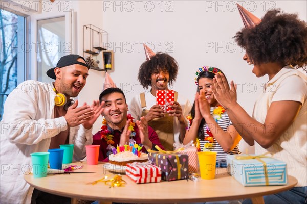 Multi-ethnic group of friends at a birthday party on the sofa at home with a cake and gifts