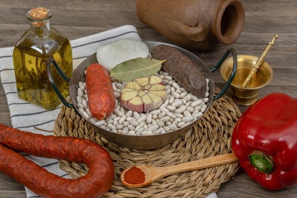 Raw white beans in metal casserole with all the ingredients for cooking them