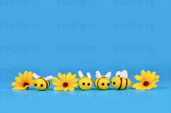 Cute felt bees and yellow flowers in a row on blue background with copy space