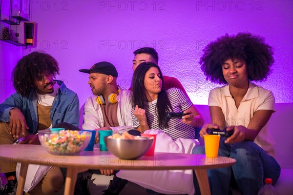 Adult party. Young people sitting on the sofa playing video games with popcorn. Joystick or controller in hand