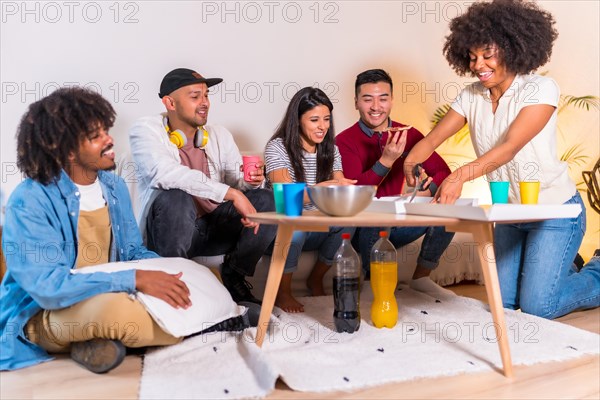 Group of multiethnic friends on a sofa eating pizza and drinking soft drinks at a home party