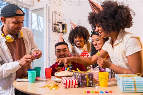 Multi-ethnic group of friends at a birthday party on the sofa at home with a cake and gifts